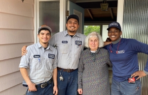 Three experts from Caccia Plumbing stand next to a happy homeowner near her front door.