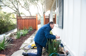 A plumber leans down to inspect pipes and valves just outside of a residence in San Mateo, California