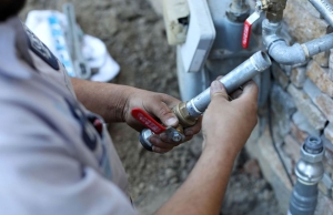 An expert from Caccia Plumbing prepares to adjust a gas supply line on the side of a house.