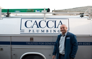 An expert plumber from Caccia Plumbing stands smiling next to a truck, ready to help with an automatic seismic shutoff valve retrofit.