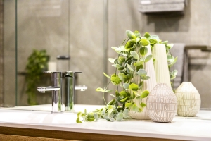 Decorative pots and vases sit on a counter to the right of a bathroom sink with a silver faucet. Eucalyptus leaves spill out of the two tallest vases.