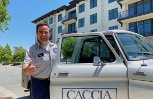 Image of Geno from Caccia Plumbing stepping out of the passenger side of a work truck and giving the thumbs-up on a sunny street corner