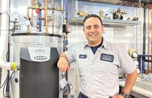 Geno from Caccia Plumbing stands beside a new water heater installation.