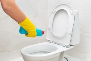 Homeowner pouring bio-cleaner into clogged toilet before calling plumber