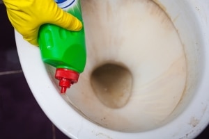 Homeowner pouring soap into clogged toilet before flushing with hot water