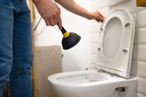 Homeowner using plunger to unclog toilet before calling plumber