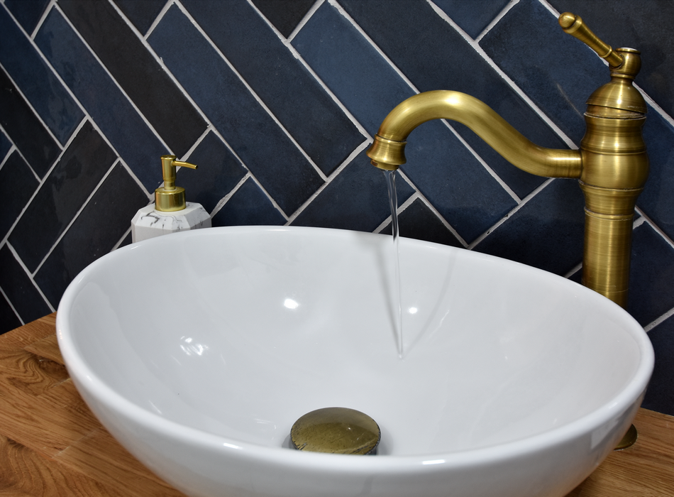 Side view of a fancy white porcelain bathroom sink with a freestanding bowl and brushed bronze fixtures. Water is slowly pouring out of the tap into the drain.