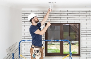 An electrician installs a new ceiling lamp in a customer's home.