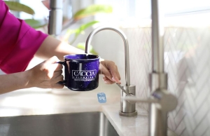 A woman adds water from a faucet to her Caccia Plumbing mug.