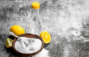 A bowl of baking soda sits beside a container of vinegar and two lemons, the perfect drain cleaning mix