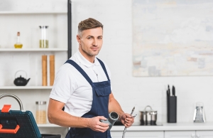 adult repairman holding pipes for kitchen faucet repairing and looking at camera