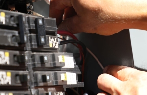 The hands of an electrician work on the wiring of an electrical panel.