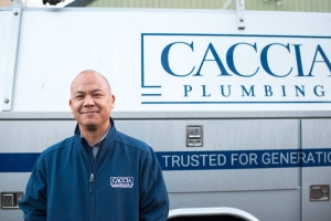 Plumber from Caccia Plumbing stands smiling outside of his work van, ready to help.