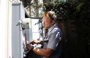 Caccia Home Services technician checking meter and electrical panel on outdoor wall of home in California