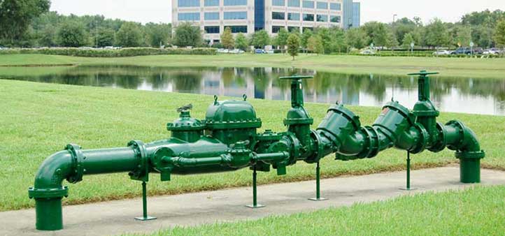 Large, green backflow preventer outdoors by a lake