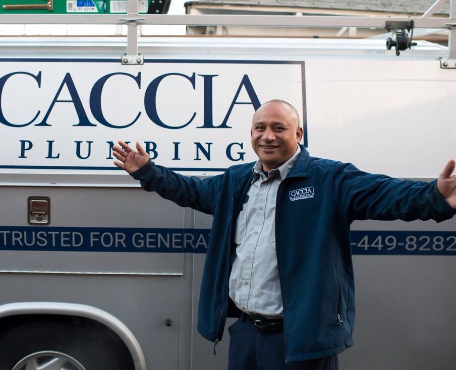 Caccia Plumbing technician smiling in front of service van, with arms outstretched to either side.