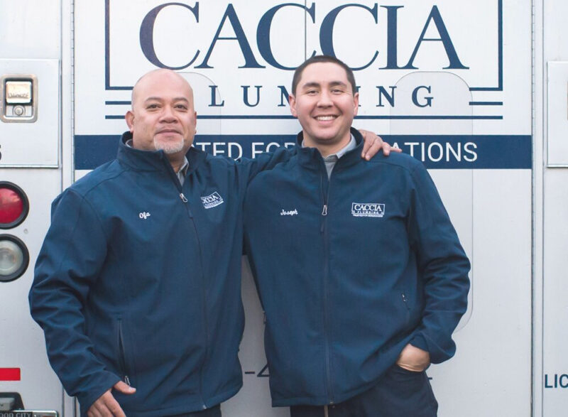 Two Caccia Plumbing plumbers standing together smiling in front of a service truck