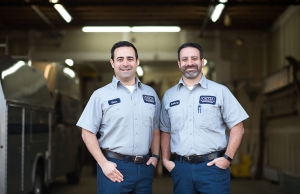 Geno and Anthony stand smiling at home base, ready to take the next plumbing, electric, or HVAC call.