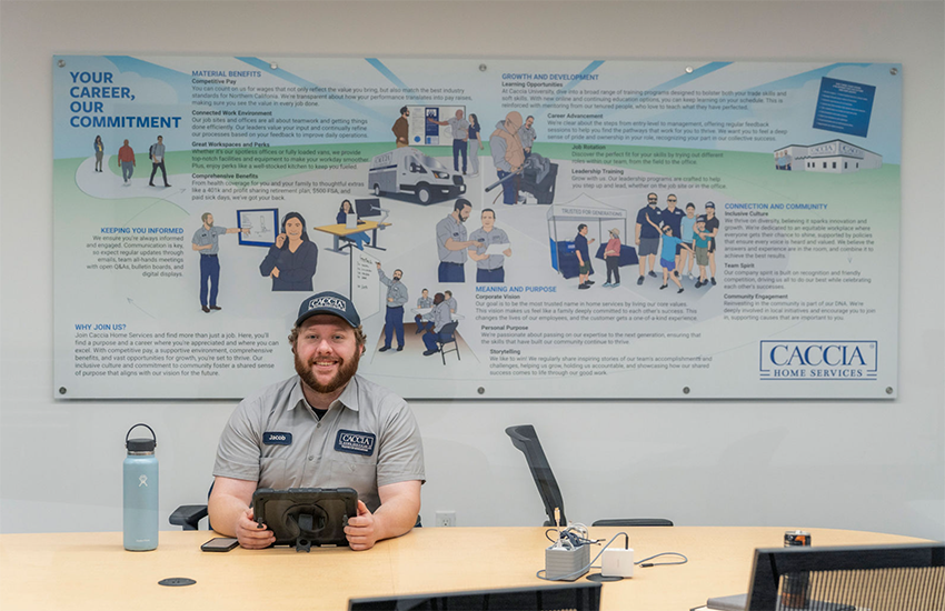 A Caccia employee sits at the career desk in front of a large banner showing the benefits of working with Caccia.