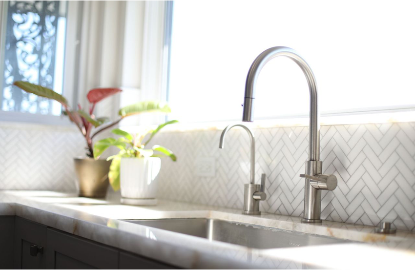 Side view of a white marble kitchen countertop and brushed nickel farmhouse-style faucet
